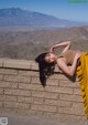 A woman leaning against a brick wall with mountains in the background.