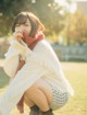 A woman in a white sweater and a red scarf sitting on the grass.