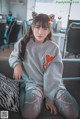 A woman sitting on a couch wearing a gray sweatshirt with a cat ears headband.