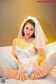 A woman in a wedding dress sitting on a bed.