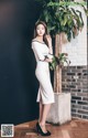 A woman in a white dress standing next to a plant.