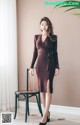 A woman in a brown dress standing next to a chair.