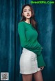 A woman in a green sweater and white skirt posing for a picture.