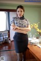 A woman standing in front of a table with her arms crossed.