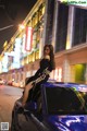 A woman sitting on top of a blue car on a city street.