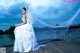 A woman in a wedding dress sitting on a dock.