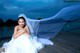 A woman in a wedding dress sitting on a dock.