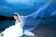 A woman in a wedding dress sitting on a dock.