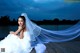 A woman in a wedding dress sitting on a dock.