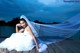 A woman in a wedding dress sitting on a dock.