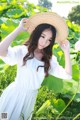 A woman in a white dress and straw hat standing in a field of flowers.