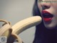 A woman with red lipstick holding a banana in front of her mouth.