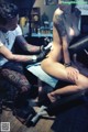 A woman getting a tattoo on a man's leg.